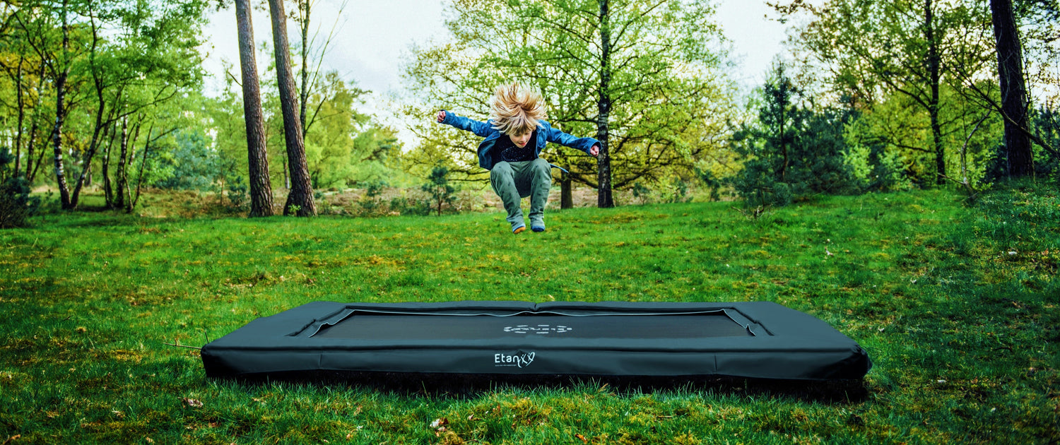 Etan Inground trampoline antraciet, in het bos met springende jongen