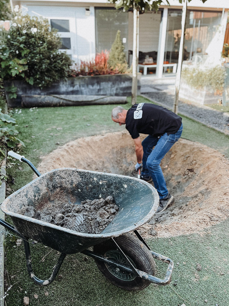 Etan medewerker graaft een trampoline kuil in een tuin met schep en kruiwagen