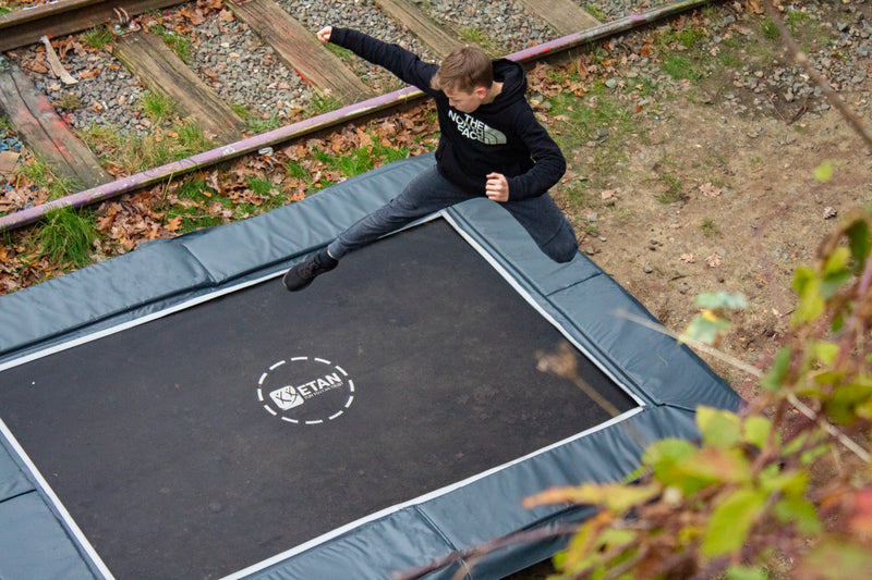 Etan UltraFlat trampoline antraciet naast treinspoor met springende jongen