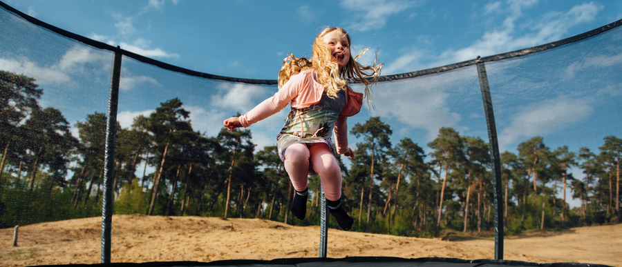 Vrolijk meisje springend op een trampoline met veiligheidsnet in de natuur